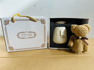 Lote #020 - Dos cajas para regalería que c/u contiene: una taza en cerámica esmaltada de color + cuchara color oro + toalla pequeña (color blanco)